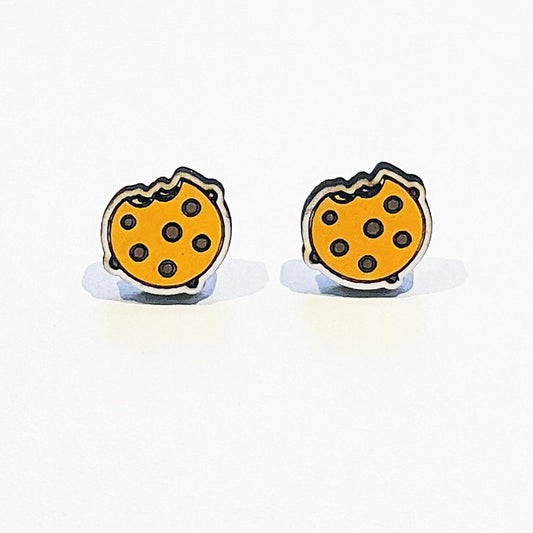 A pair of handmade stud earrings shaped like chocolate chip cookies, each featuring a playful bite mark on the top edge. The cookies are round with a golden-brown colour and scattered dark brown chocolate chips. The earrings have a whimsical, cartoon-style design with a glossy finish, and they sit against a clean white background. Perfect for fans of cute food-themed accessories or lovers of sweet treats with a quirky, fun flair.