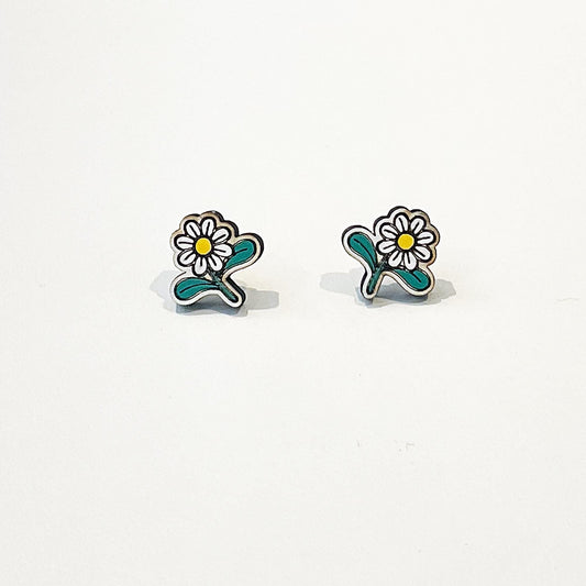 A pair of small, handcrafted stud earrings shaped like daisy flowers. Each earring features white petals with a yellow centre and two green leaves, set against a plain white background. The earrings are symmetrically designed, lightweight, and have a playful, nature-inspired look. Perfect for spring or summer, they add a cute and feminine touch to any outfit, making them ideal for those who love floral or cottagecore-themed accessories.