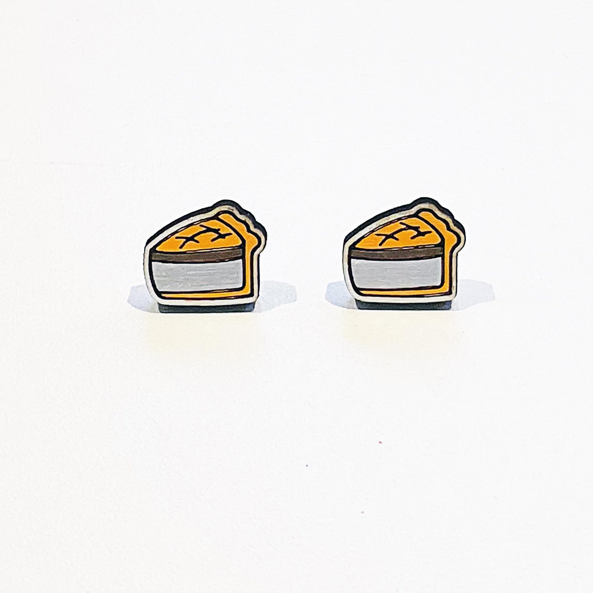 A pair of handmade stud earrings shaped like classic British pork pies. Each earring features a detailed slice of golden-brown pork pie with a crimped pastry edge and visible meat filling, outlined in black for a bold, cartoon-style finish. The design is flat with a glossy surface and stainless steel posts attached at the back. The earrings are displayed against a plain white background with soft shadows beneath them.