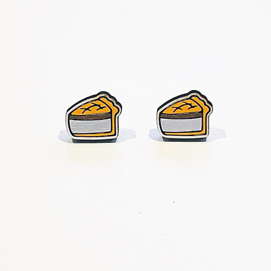 A pair of handmade stud earrings shaped like classic British pork pies. Each earring features a detailed slice of golden-brown pork pie with a crimped pastry edge and visible meat filling, outlined in black for a bold, cartoon-style finish. The design is flat with a glossy surface and stainless steel posts attached at the back. The earrings are displayed against a plain white background with soft shadows beneath them.